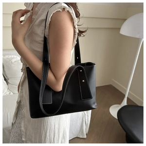 Detail of black faux leather tote bag with white contrast stitching and gold rivets