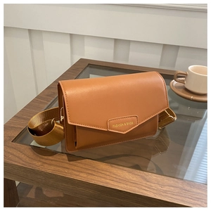 Detail of brown crossbody bag with wide strap and fashion logo on glass table