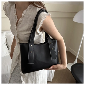 Detail of black leather tote bag with white contrast stitching and gold rivets