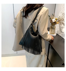 Detail of black pebbled leather bucket bag featuring long fringes and gold metal eyelets