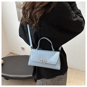 Detail of light blue crossbody bag with crocodile texture and metal handle on model