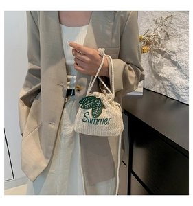 Detail of cream straw bucket bag featuring green leaf patch and Summer embroidery