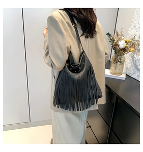 Detail of black pebbled leather tote bag featuring long fringes and gold metal hardware