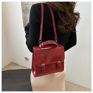 Rear view of model wearing a glossy red retro satchel with dual buckle straps and top handle