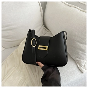 Detailed shot of a black glossy shoulder bag with a rectangular gold buckle and metal strap buckle