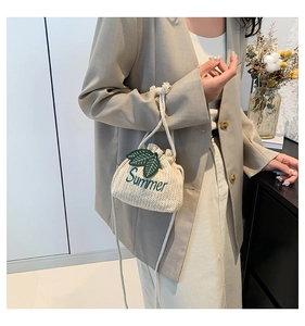 Detail of cream woven bucket bag featuring green Summer embroidery and drawstring closure