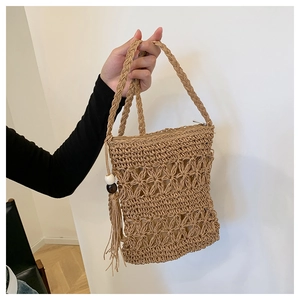 Detail of bohemian straw bag featuring hollow floral pattern, tassels and dual handles