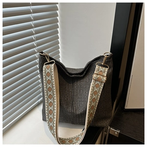 Détail d'un sac à bandoulière tressé noir avec sangle brodée et finitions dorées