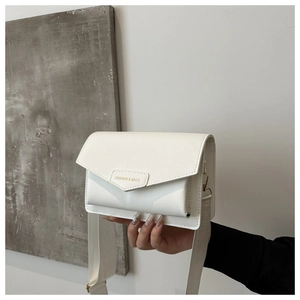 Detail of white envelope crossbody bag featuring gold metal nameplate and wide strap