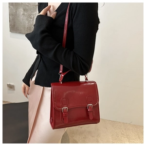 Detail of a dark red patent leather crossbody bag with silver buckles on a model