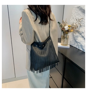 Side view of black leather shoulder bag with long fringes and metal eyelet details