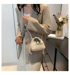 Detail of straw bucket bag with green leaf embroidery and Summer text on woven fabric