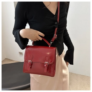 Close-up of a glossy red crossbody bag featuring metallic buckle and adjustable strap