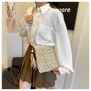 Detail of straw woven crossbody bag featuring tassels and wooden beads on a white pedestal