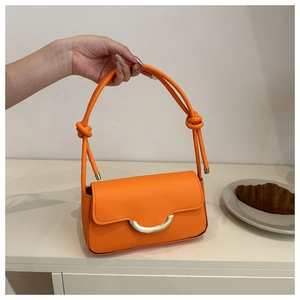 Détail d'un petit sac carré orange vif avec une boucle métallique dorée en demi-lune chic