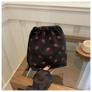 Détail d'un sac seau en velours côtelé noir avec imprimé fraise tenu à la main