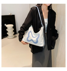 Detail der weißen Leder-Schultertasche mit blauem Schmetterlingsmuster und Kette