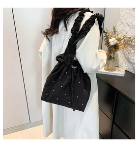 Detail of black tote bag featuring ruffle shoulder strap and pearl embellishments