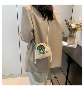 Detail of beige straw bucket bag with green Summer embroidery and rope strap