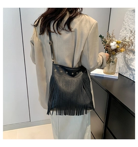 Detail of black fringe shoulder bag with gold metal eyelets shown on a model