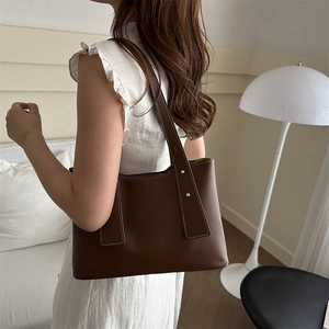 Minimalist brown leather shoulder bag with white contrast stitching and gold rivets