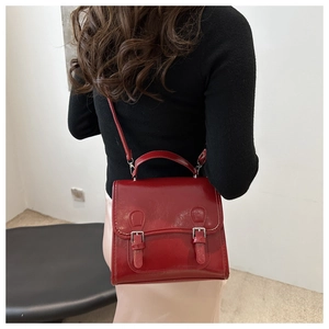 Rear view of model holding a glossy red vintage handbag with decorative buckles