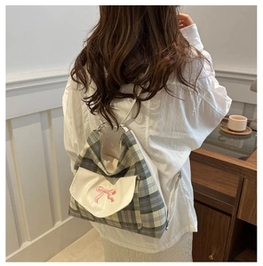 Close-up of blue plaid backpack featuring a white flap with a pink embroidered bow detail