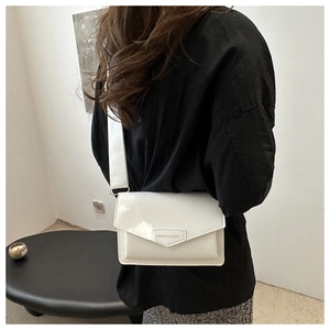 Close-up of white patent leather crossbody bag showing the metallic logo and wide strap