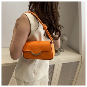 Détail d'un sac bandoulière en cuir orange mat avec boucle argentée et bandoulière nouée