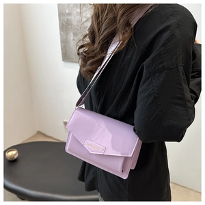 Close-up of lilac patent leather crossbody bag with gold text and wide strap on model