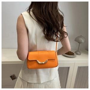 Détail du sac baguette orange vif avec fermoir doré en demi-lune sur un modèle