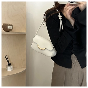Detail of white baguette bag featuring a gold crescent buckle and knotted shoulder strap