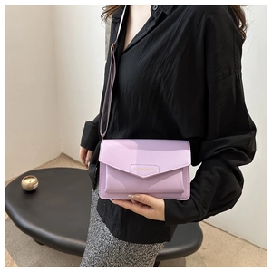 Lavender small crossbody bag detail with golden logo worn with a black shirt and grey skirt