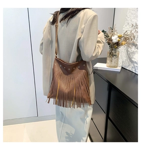 Detail of a brown fringe tote bag with matte leather texture and metal eyelets