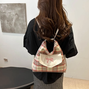 Pink and green plaid backpack with embroidered bow detail and front pocket on person