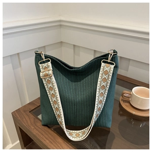 Detailed view of dark green textured bucket bag with embroidered geometric wide strap