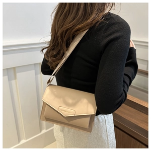 Side view of beige leather crossbody bag with wide strap worn by a model in interior