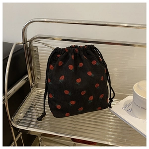 Détail du sac à cordon en velours côtelé noir avec imprimé fraises sur une étagère