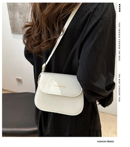 Model wearing a white glossy leather saddle bag with gold lettering and flap design