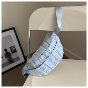 Détail d'un sac banane rayé bleu et violet suspendu à une chaise blanche minimaliste