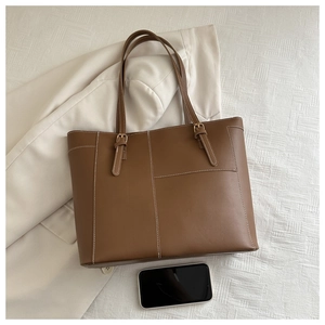 Cabas en cuir marron avec surpiqûres et boucles, présenté à côté d'un téléphone pour l'échelle