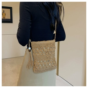 Detail of bohemian straw crossbody bag featuring intricate openwork weave and tassel accent