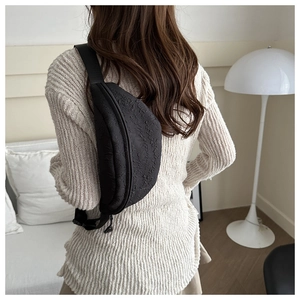 Detail of black textured bubble fabric crossbody bag with adjustable strap worn on back
