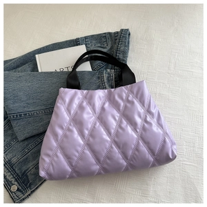 Vue à plat d'un sac cabas matelassé lilas avec anses noires et veste denim
