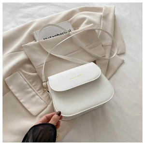 Close-up of beige PU leather saddle bag with gold logo on a cream blazer background