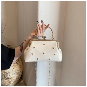 Dettaglio clutch perla crema con rivetti a cuore, manico ornato e catena dorata