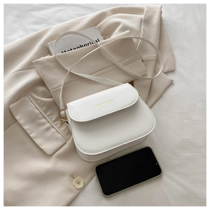 Close-up of minimalist white leather crossbody bag with golden fashion logo engraving
