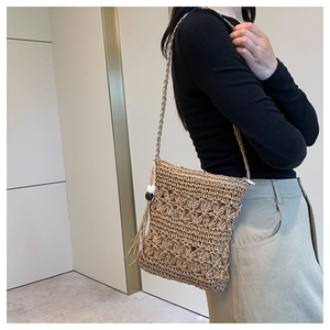 Detail of bohemian straw bag featuring hollow floral pattern and black-white bead tassels