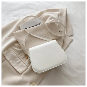 Close-up of minimalist white leather saddle bag with gold D-ring hardware on beige blazer