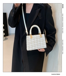 Close-up of white and gold tweed texture on elegant crossbody bag with woven handle